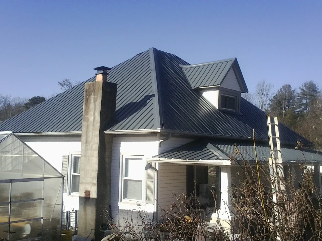 Dark blue standing seam metal roof on a white farmhouse with dormer — Slate & Tile Roof Repair by Roofing Brothers in Reva