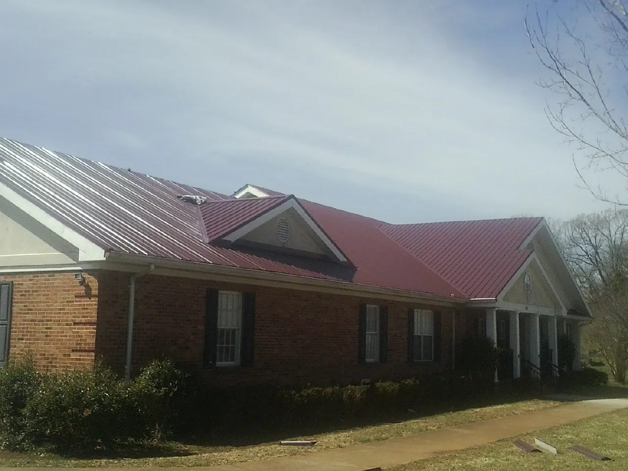 Red metal roof with gabled entries on a long brick building, from a Hail Damage Roof Repair job in Reva