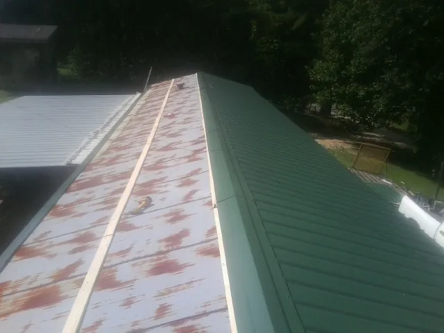 Old rusted panels beside newly installed green metal roofing — Wind Damage Roof Repair by Roofing Brothers in Reva