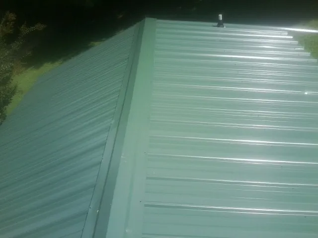 New green metal panels meeting at the ridge of a roof — Flat Roof Repair work by our crew in Reva