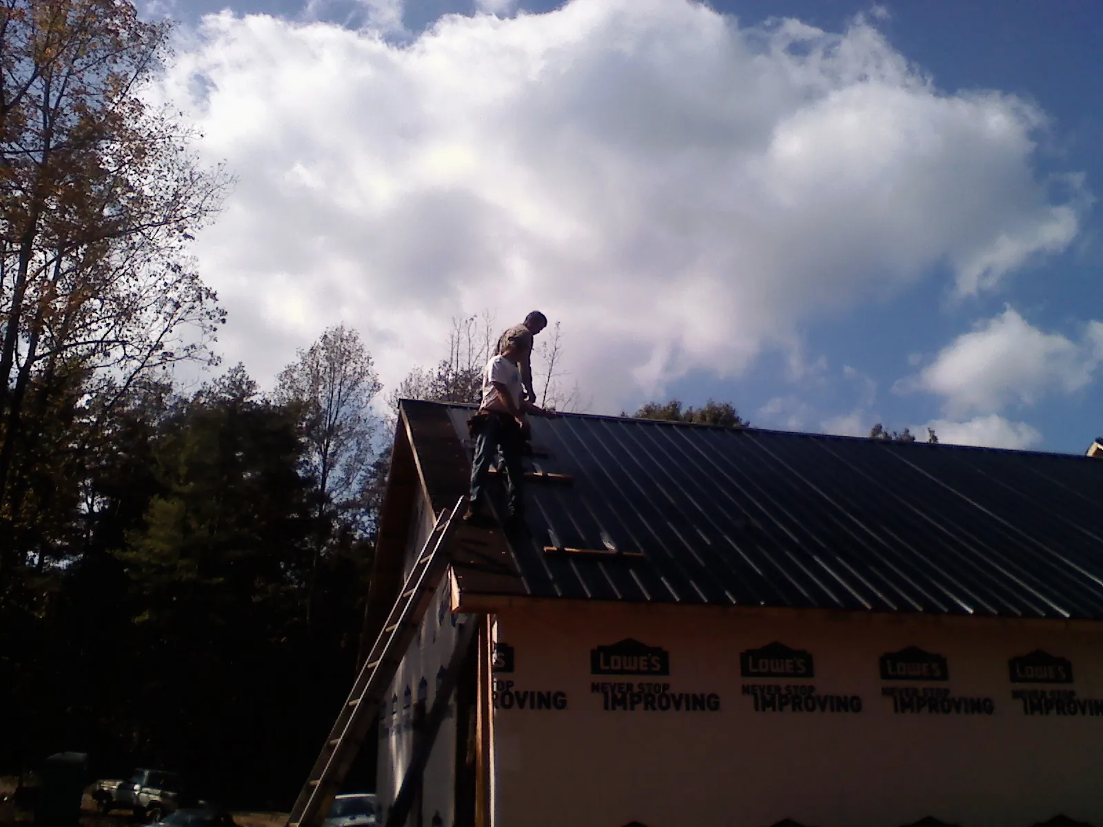 Roofer fastening dark metal panels high against a cloudy sky, from a Roof Inspection job in Reva