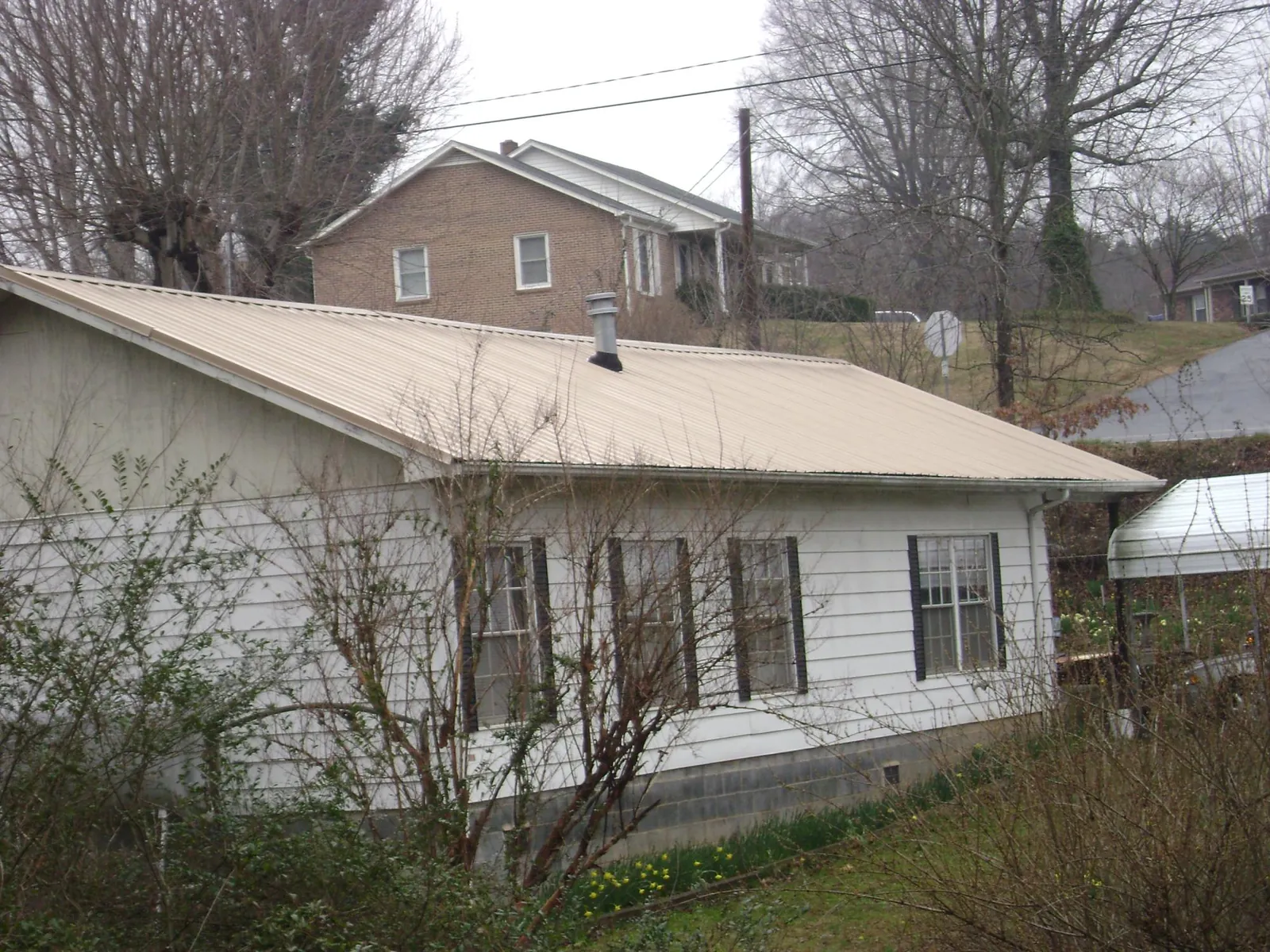 Tan metal roof on a white sided house set into a hillside — Commercial Roofing by Roofing Brothers in Reva