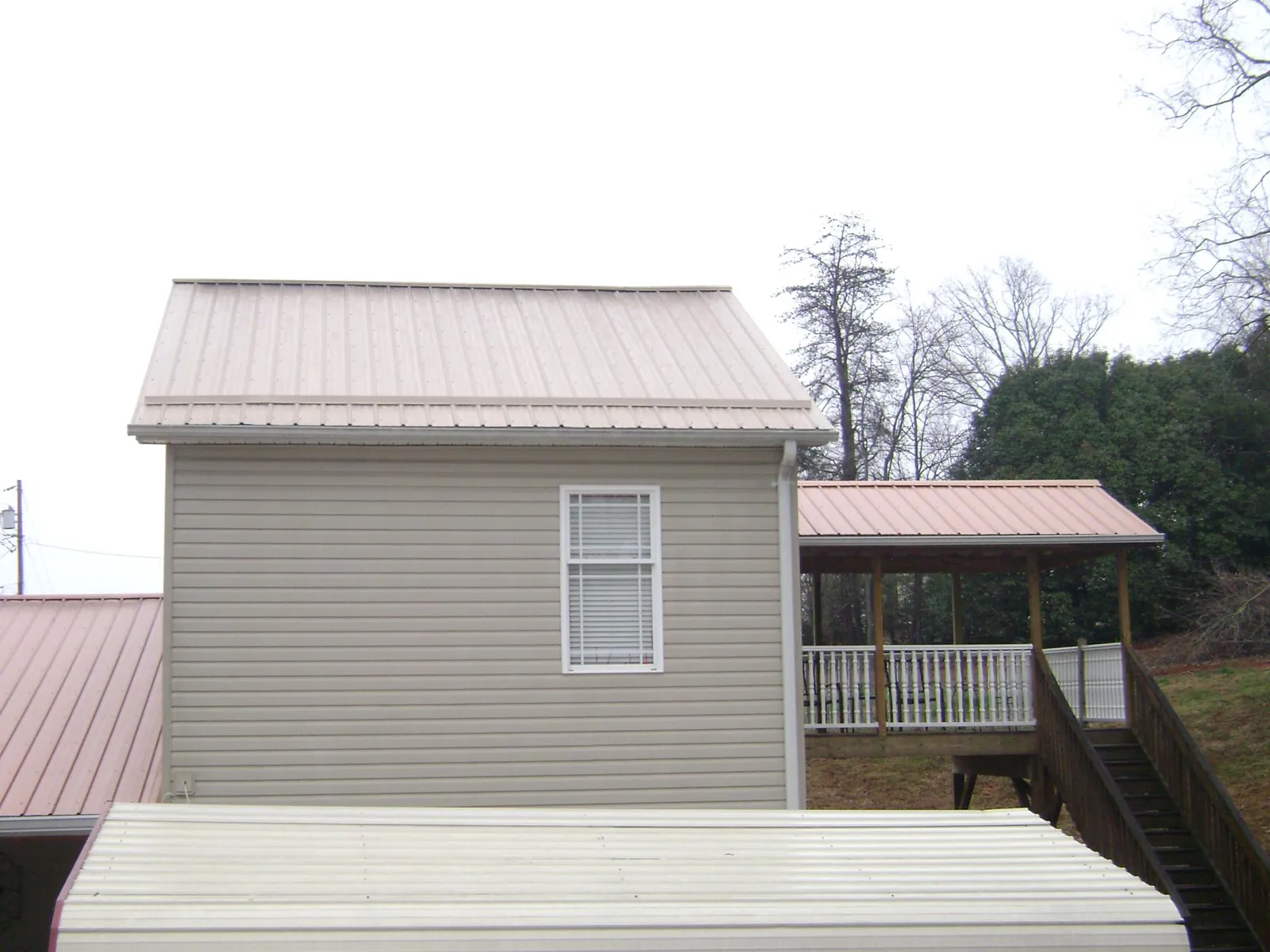 Tan metal roofs on a two story addition and attached porch, from a Roof Replacement job in Reva